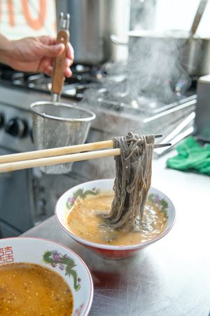 Cook preparing tasty dish with noodles and broth