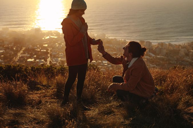 Young man kneeling and proposing woman with wild flower on mountain