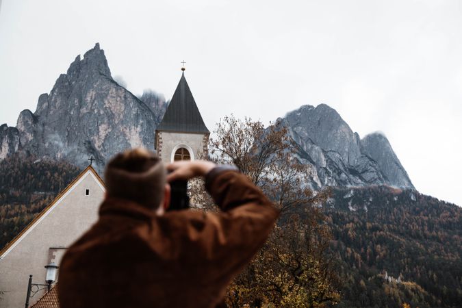 Male traveler making photo of nature and church on camera