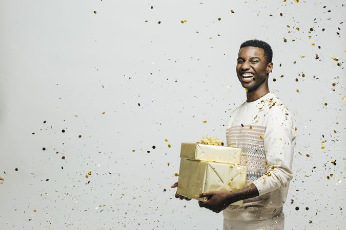 Smiling Black man holding pile of wrapped present as glitter falls