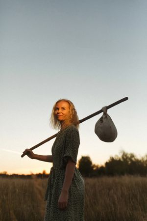 Woman standing in field with bindle at sunset
