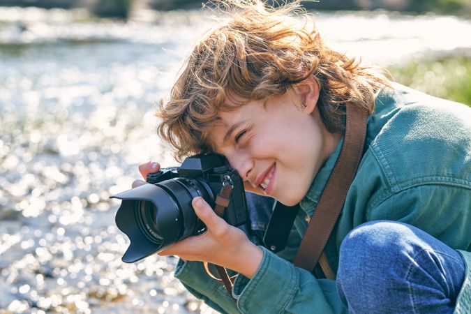 Cheerful boy taking photo on grassy coast