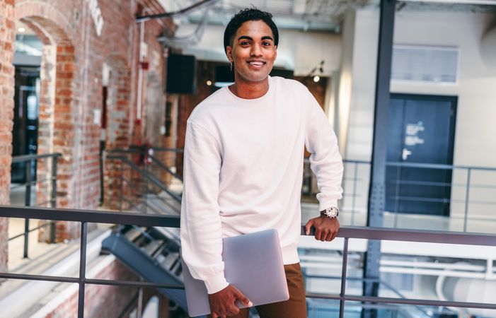 Cheerful young businessman looking at the camera in a modern workplace with brick walls