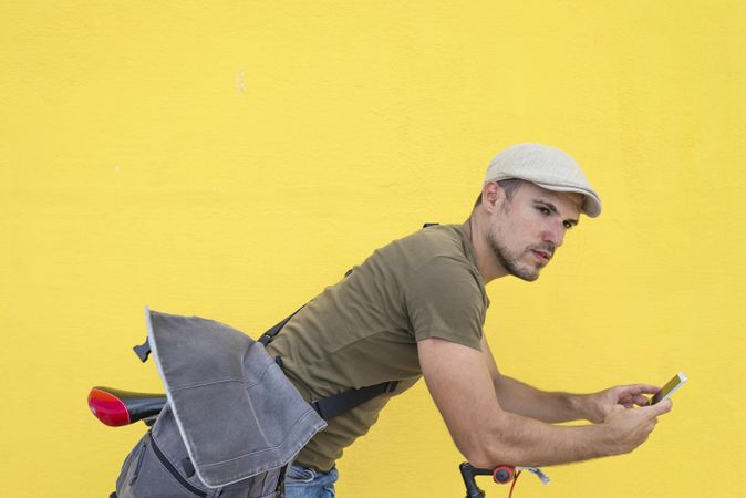 Male in hat and sunglasses looking up from phone while sitting on bicycle