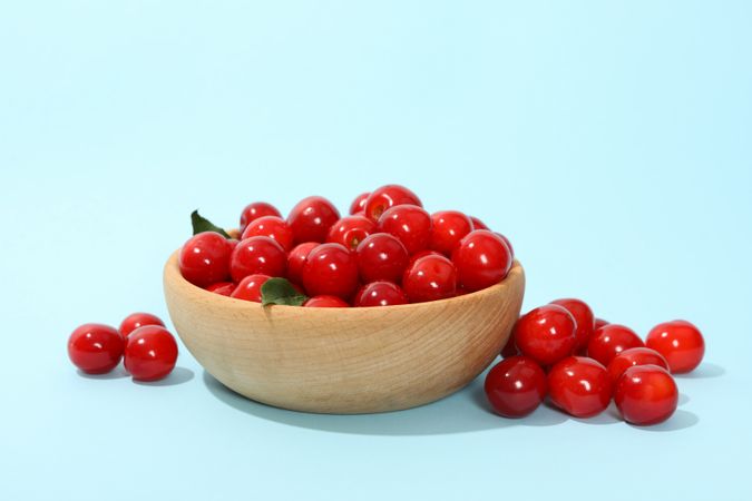 Bowl with fresh red cherry on blue background, close up