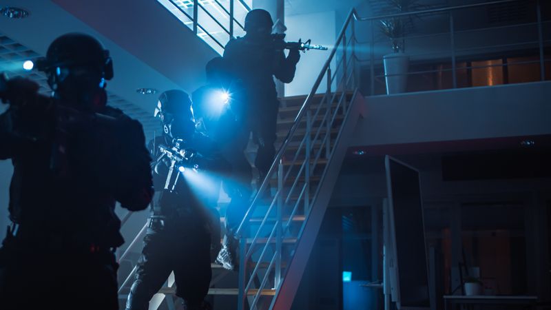 Masked Squad of Armed SWAT Police Officers Run Down the Stairs from a Second Floor in a Dark Office Building.