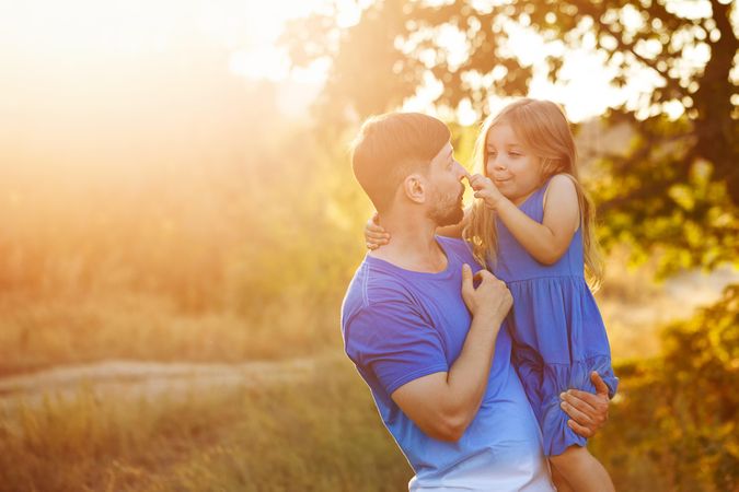 Happy man holding daughter  in sunny meadow