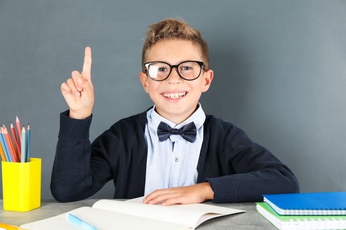 Boy in school uniform sitting at the table against board background