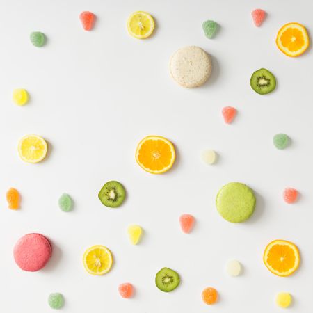 Fruit slices, gummies, and macarons on light background