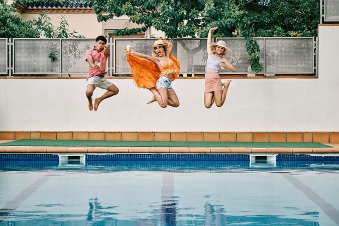 two young women and a man jumping by the pool
