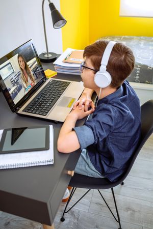 Boy with headphones receiving class at home with laptop from his bedroom