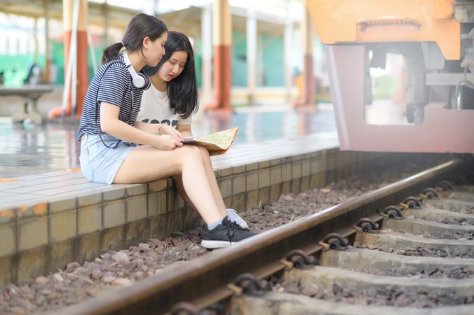 Two female travelers look at maps on a train platform