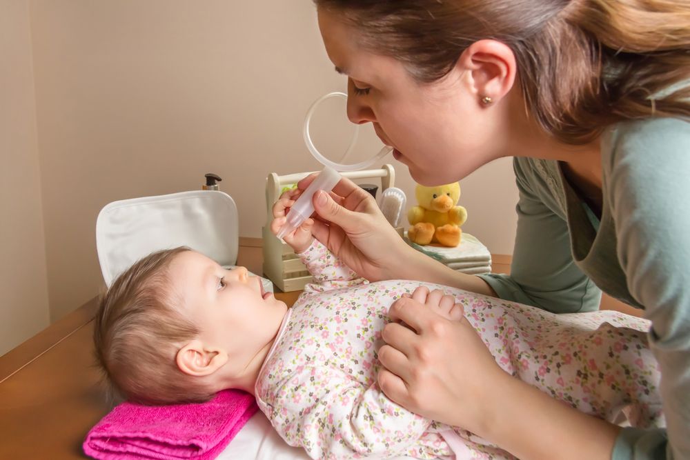Baby playing with nasal aspirator with mother