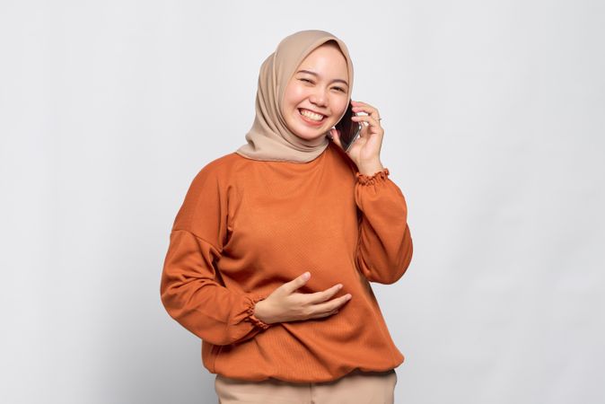 Smiling Muslim woman laughing with smart phone to her ear talking to friend