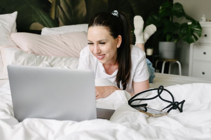 Smiling woman using laptop in bed during weekend