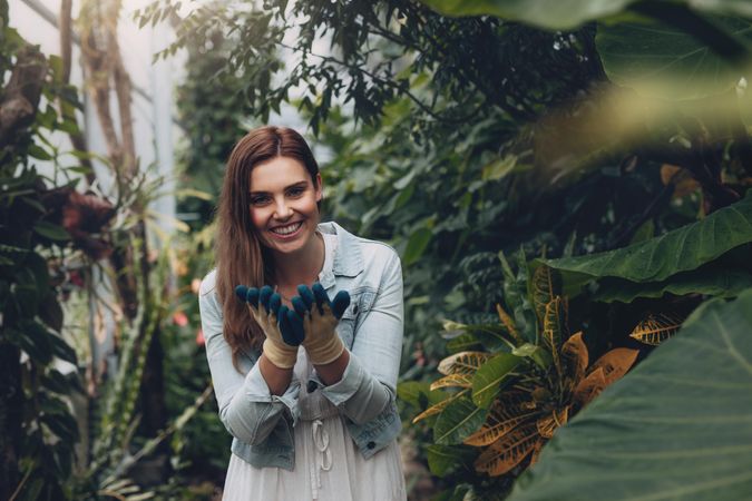 Happy woman standing in the plant nursery wearing hand gloves