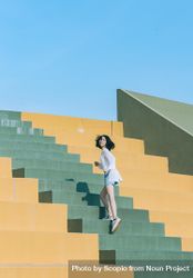 East Asian woman climbing yellow and orange staircase in sparse outdoor 0P2oe4
