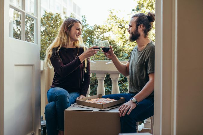 Couple sitting in their new home eating pizza and drinking wine