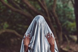 Woman holding metallic blue sheet overhead with hands on shoulders