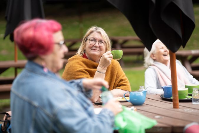 Older women sitting outside at park bench sipping tea