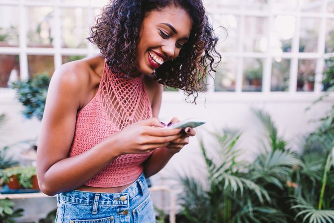 Happy young woman smiling while texting on a smartphone surrounded by plants