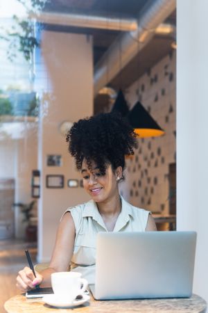 Smiling Black woman working on graphic tablet in cafe