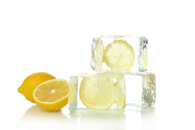 Square clear ice cubes with lemon slices, next to halved lemon