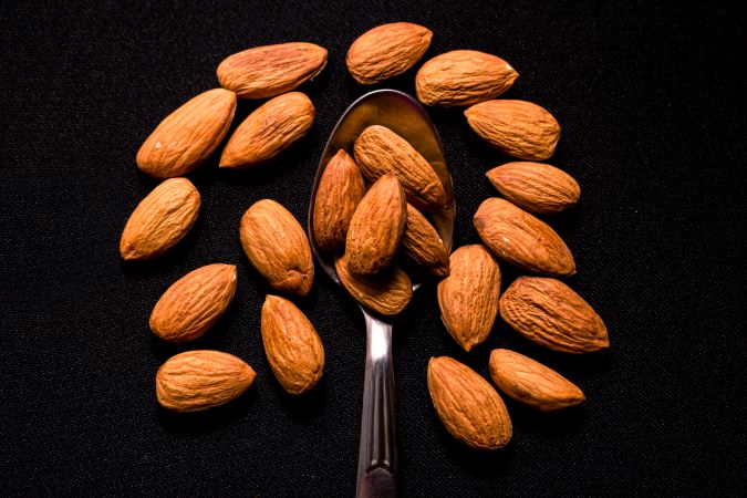 Top view of tasty almonds placed on a steel spoon on a dark background
