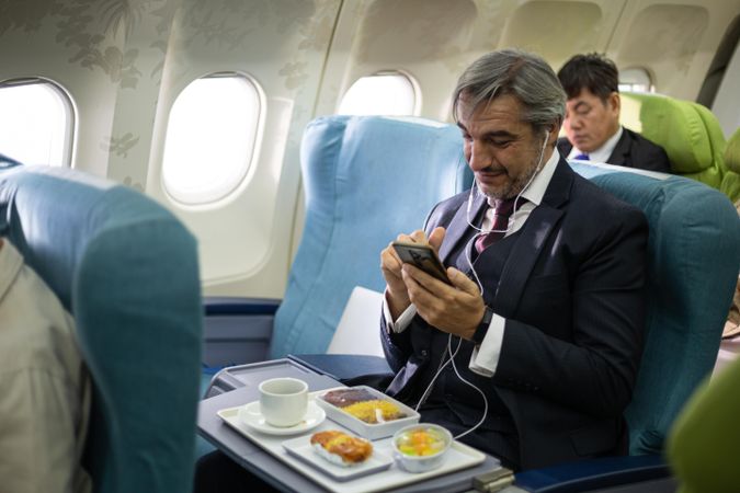 Man in suit on flight using smart phone while meal is served