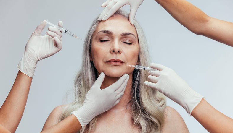 Older female getting injections by beauticians over grey background