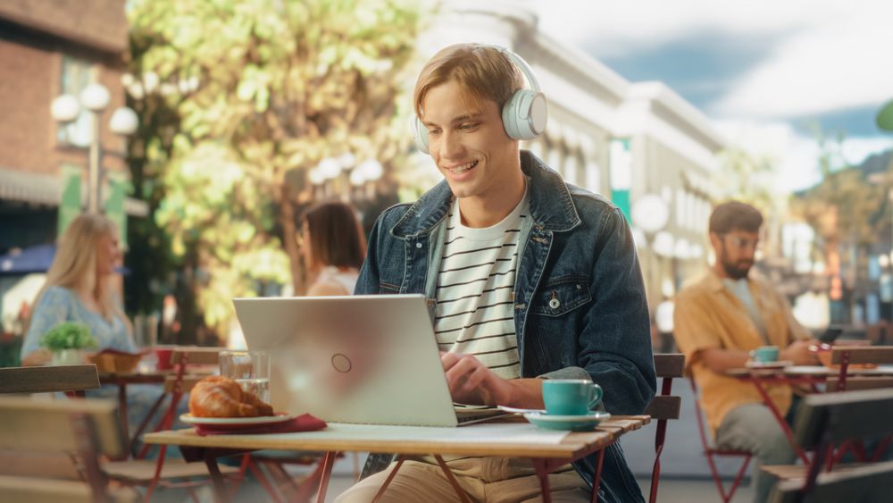 Freelancer Wearing White Headphones and Using a Laptop Computer for Remote Online Work in the City.