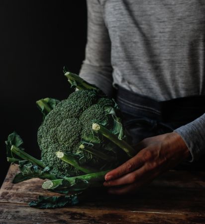 Crop woman holding fresh broccoli over table