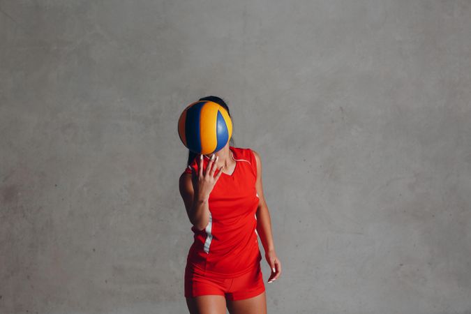 Woman in red sports uniform holding yellow and blue volleyball