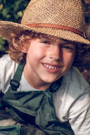 Cheerful preteen boy in wicker hat and apron