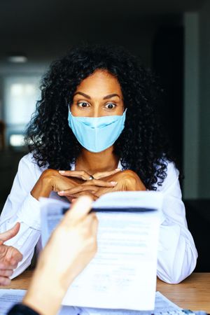 Woman looking at document a colleague is holding up wearing a facemask