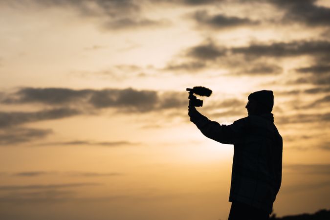 Anonymous happy woman recording vlog on camera under sundown sky