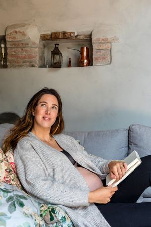 Pregnant woman lounging on sofa with book