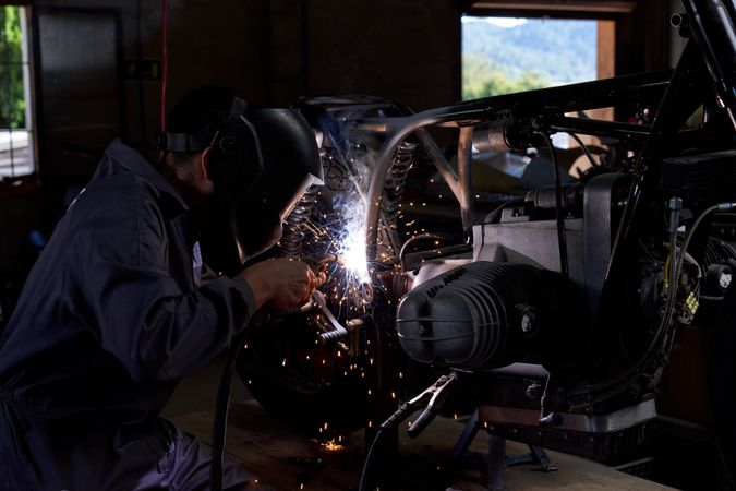 Anonymous workman using welding machine while fixing motorbike i