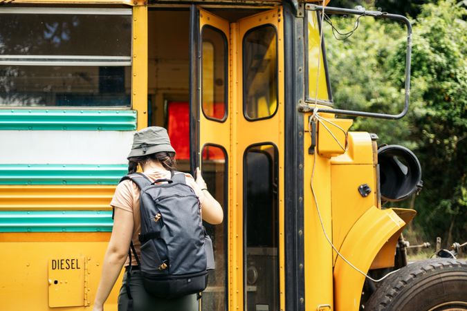 Woman with backpack entering a yellow bus