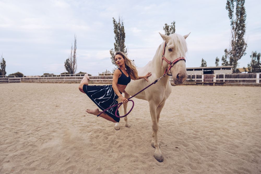 woman in skirt leaning on horse side while dancing at paddock