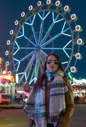 Smiling young woman near illuminated ferris wheel at night