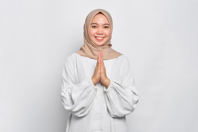 Happy Muslim woman in headscarf and light blouse with hands together in prayer