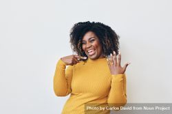 Studio shot of a happy Black woman in yellow shirt showing off her engagement ring 4772A4