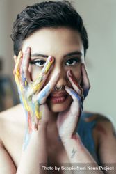 Woman with blue and yellow paint on hands covering her face bedAp4