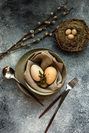 Top view of Easter holiday table setting with bowl of eggs and branch