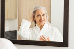 Female in bathrobe adjusting her hair in mirror