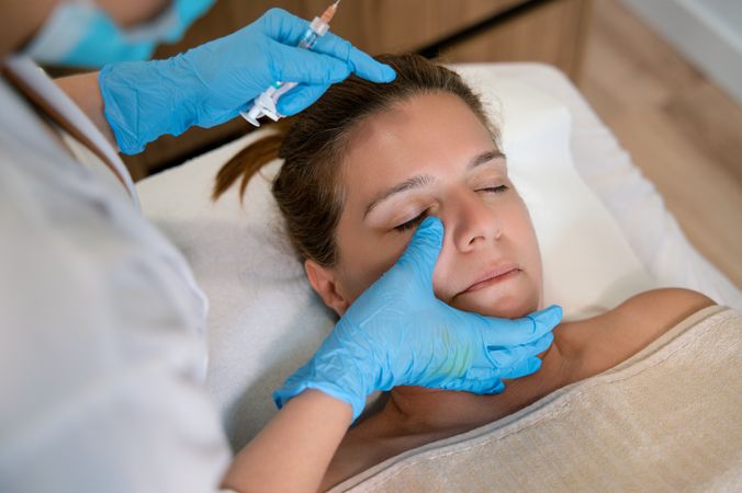 Crop cosmetologist massaging face of client in clinic