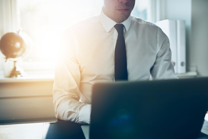 Man in shirt and tie sitting at desk and typing on laptop