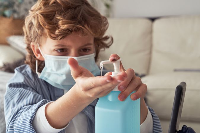 Boy in medical mask disinfecting hands with sanitizer during pan
