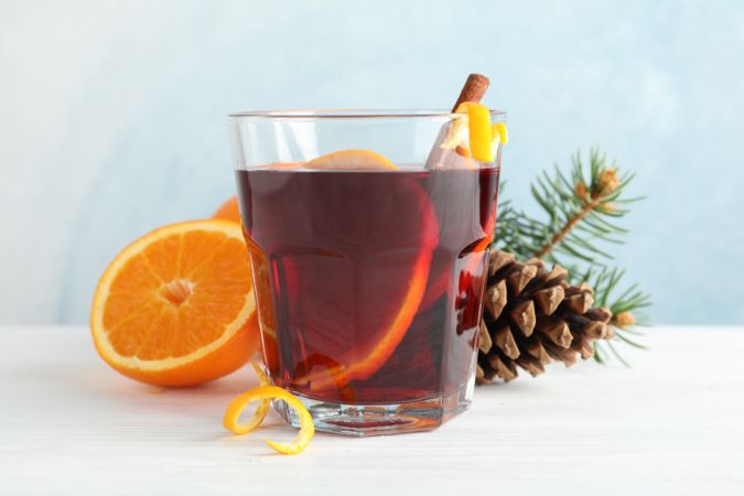 Glass of tasty mulled wine with orange on wooden background, space for text